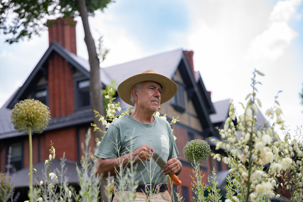 A man stands in a garden, the Inn in the background