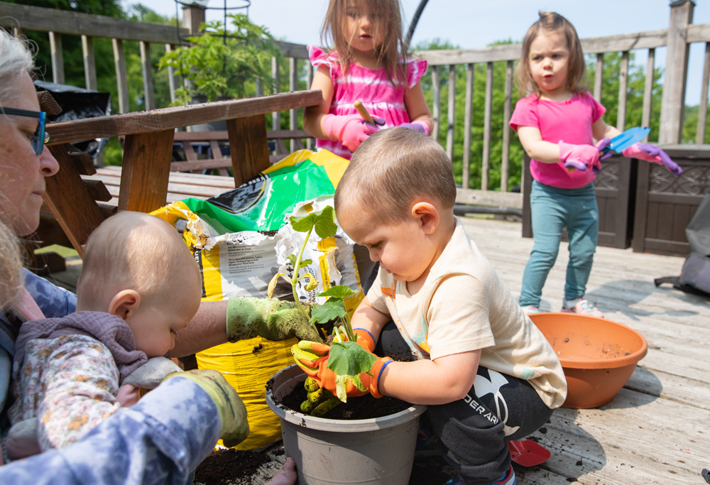 A woman plants a squash plant with a group of young children