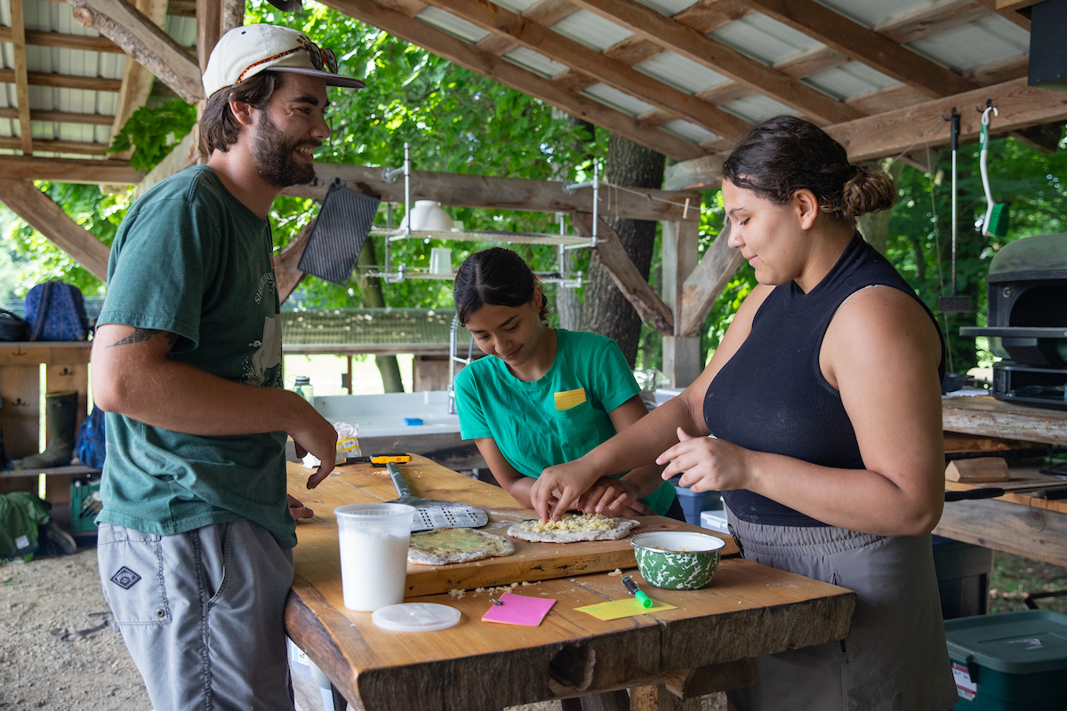 three young people making pizza in an outdoor classroom