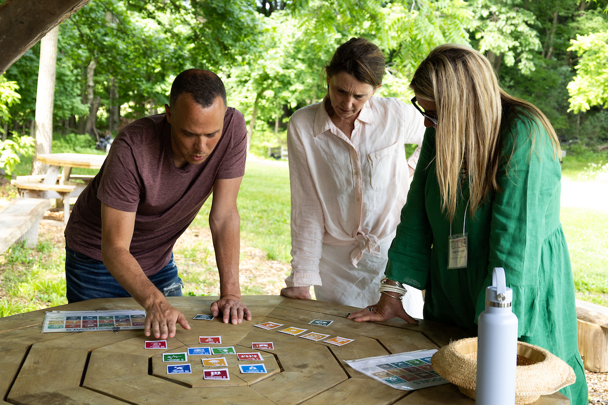 a man and two woman looking at colorful cards on an outdoor table.