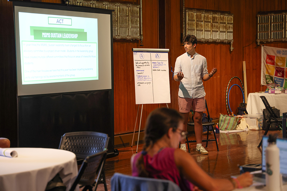 A teenaged student stands in front of a projector screen giving a presentation