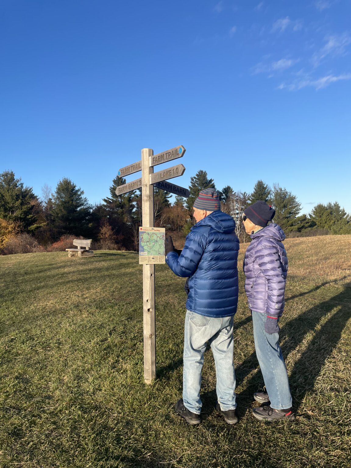 an older man and woman in jeans and winter coats looking at a walking trail sign