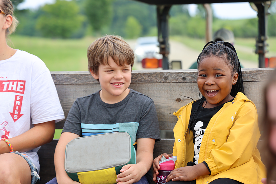 two campers smiling from a wagon