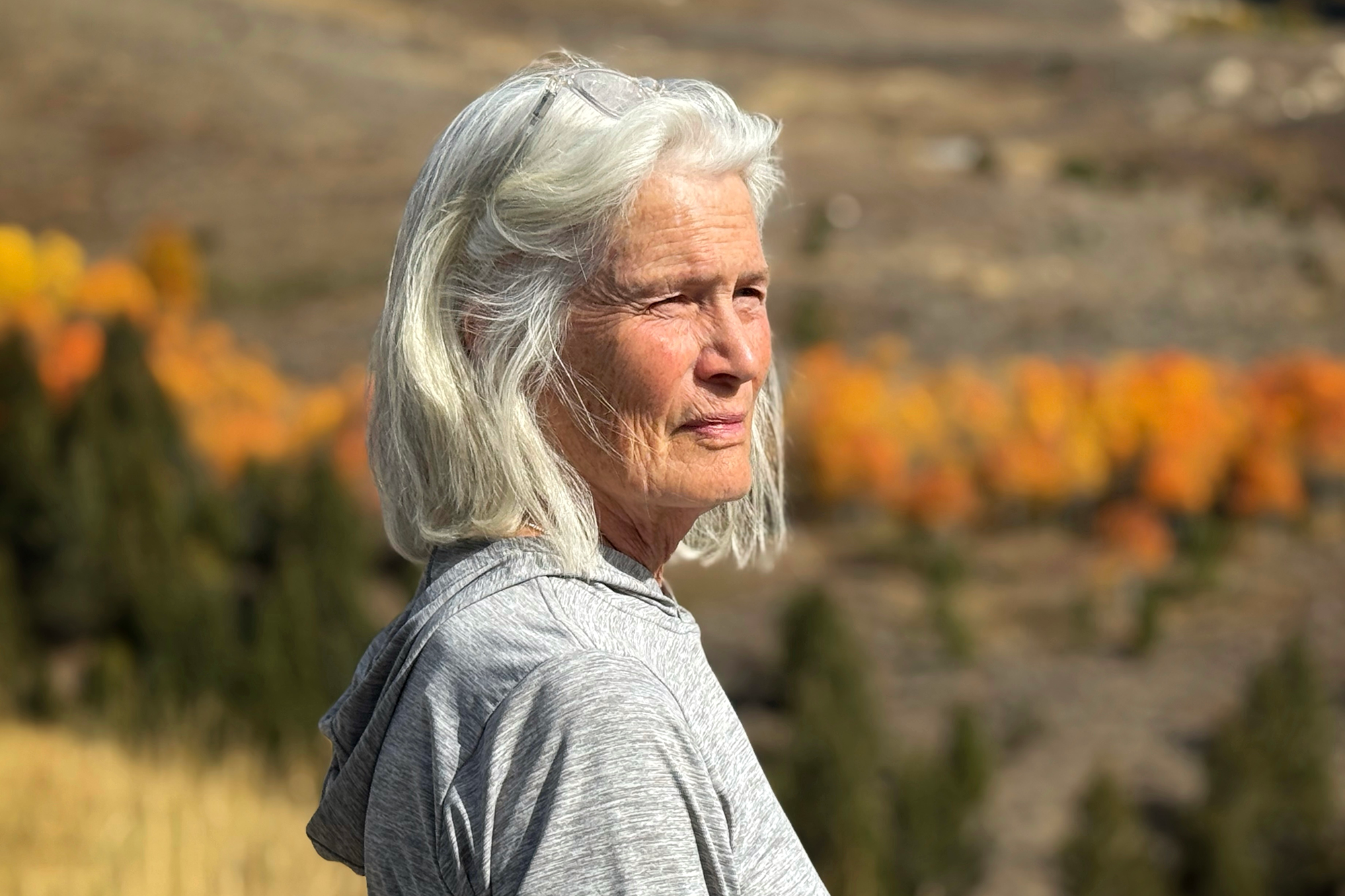 Woman with white hair photographed in an outdoor setting with orange flowers in the distance.