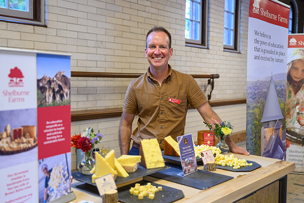 Man in short-sleeved shirt behind a table showcasing various cheeses