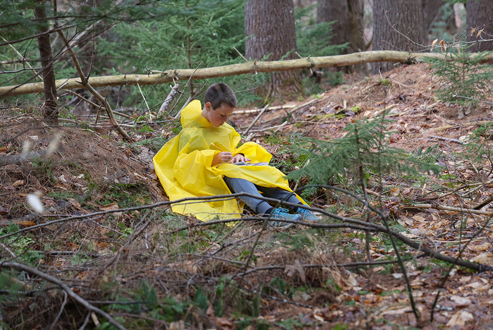 A middle school aged student writes in a notebook while sitting in the forest