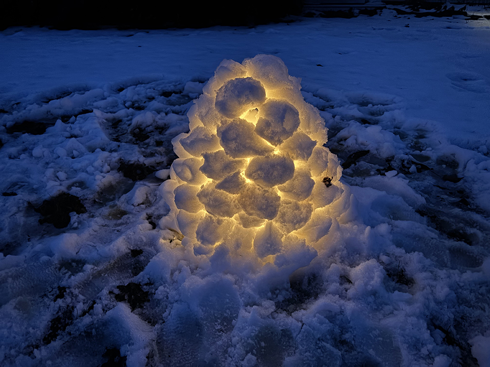 a small igloo made of snowballs with a lit candle inside at dusk.