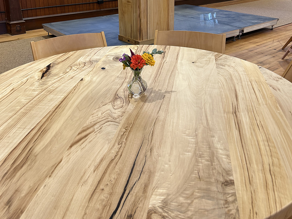 top of a round wooden table showing all the detailed wood grain. A small vase of flowers is on the table