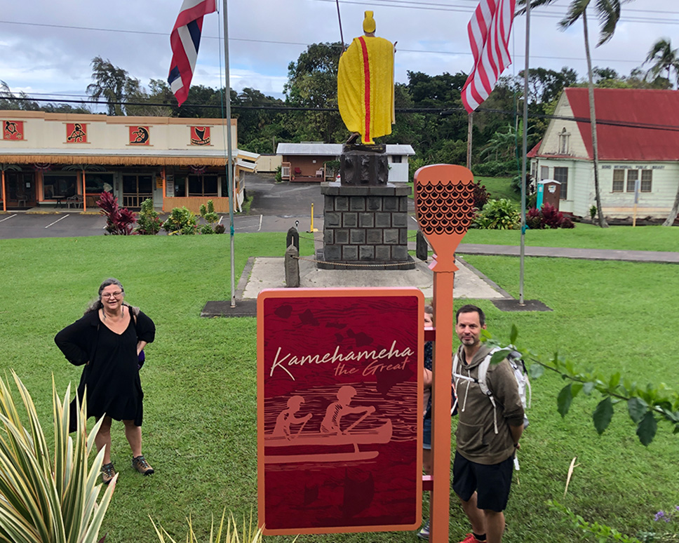 Two adults pose for camera, standing on either side of a sign at an educational center in Hawaii