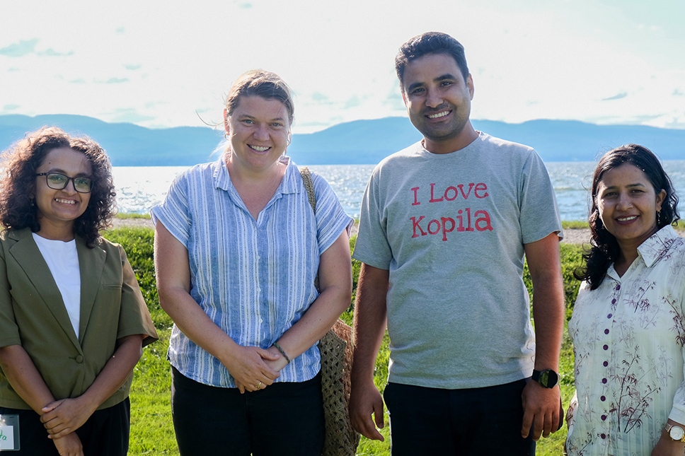 Four people pose in front of a bright lake in summertime