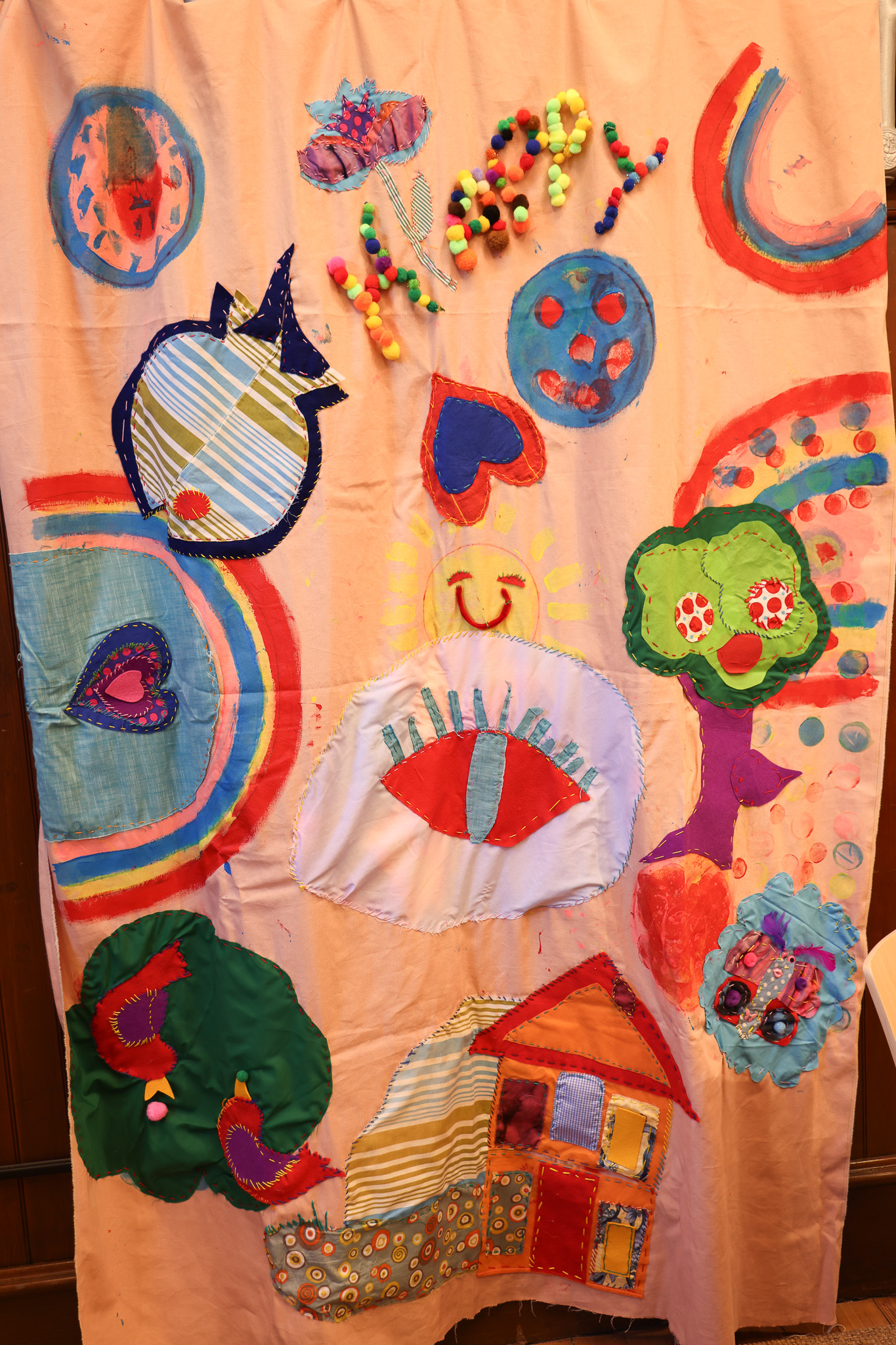 A colorful banner with handpainted and sewn elements and the word Happy