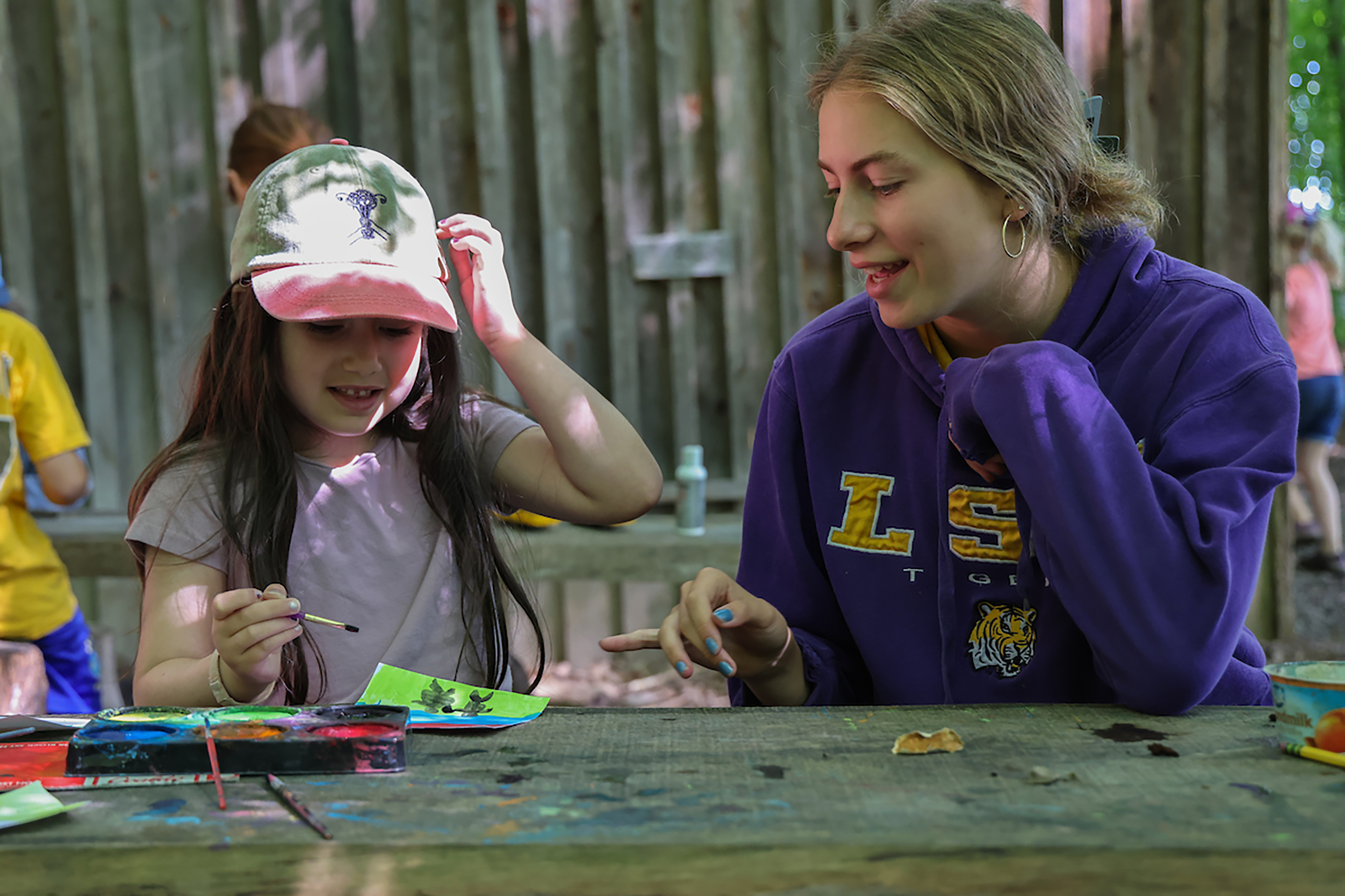 A woman and young child sit at an outdoor table painting watercolors