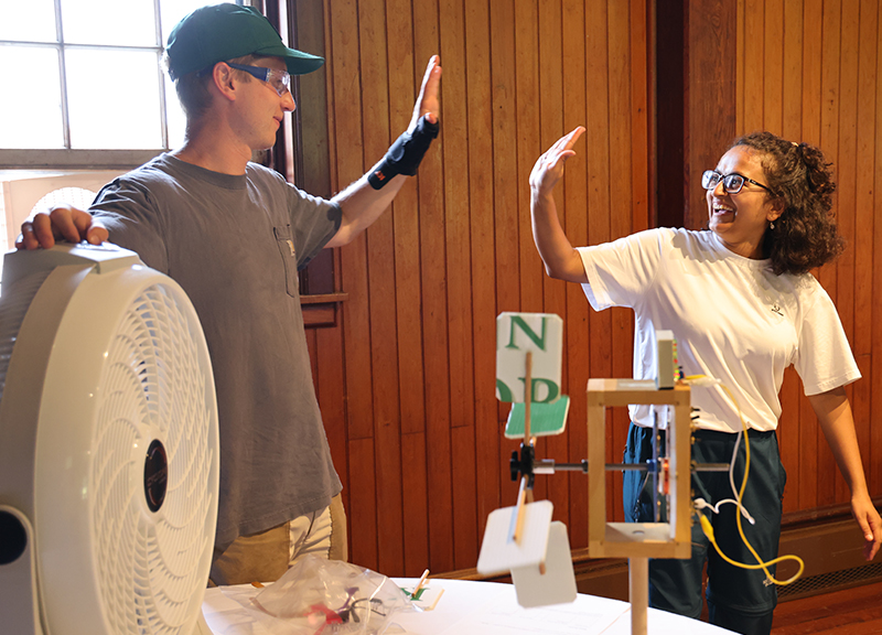 Two people high five standing around a simulated wind turbine activity.