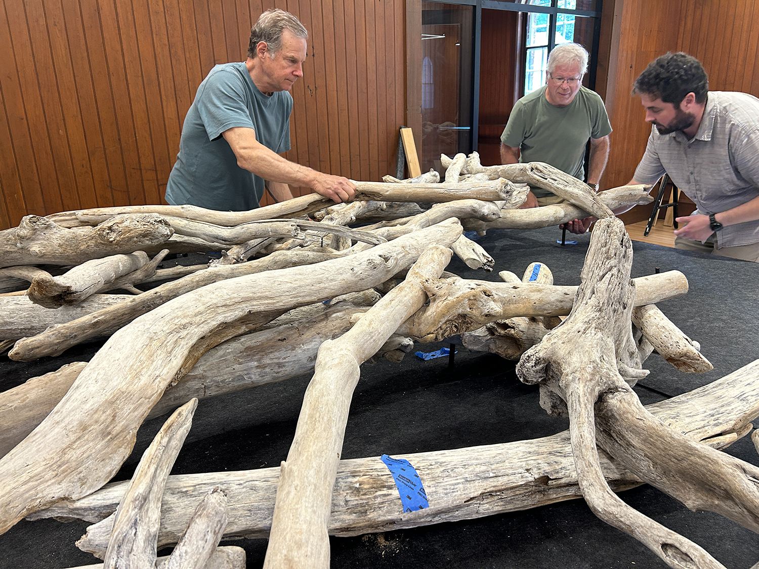 three men arrange large pieces of driftwood on a table