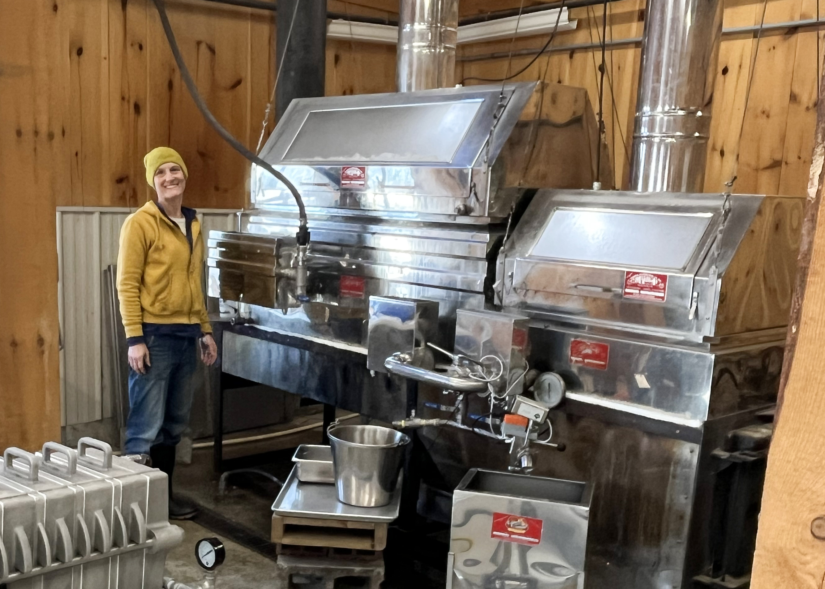 Woman standing beside maple sugaring evaporator.