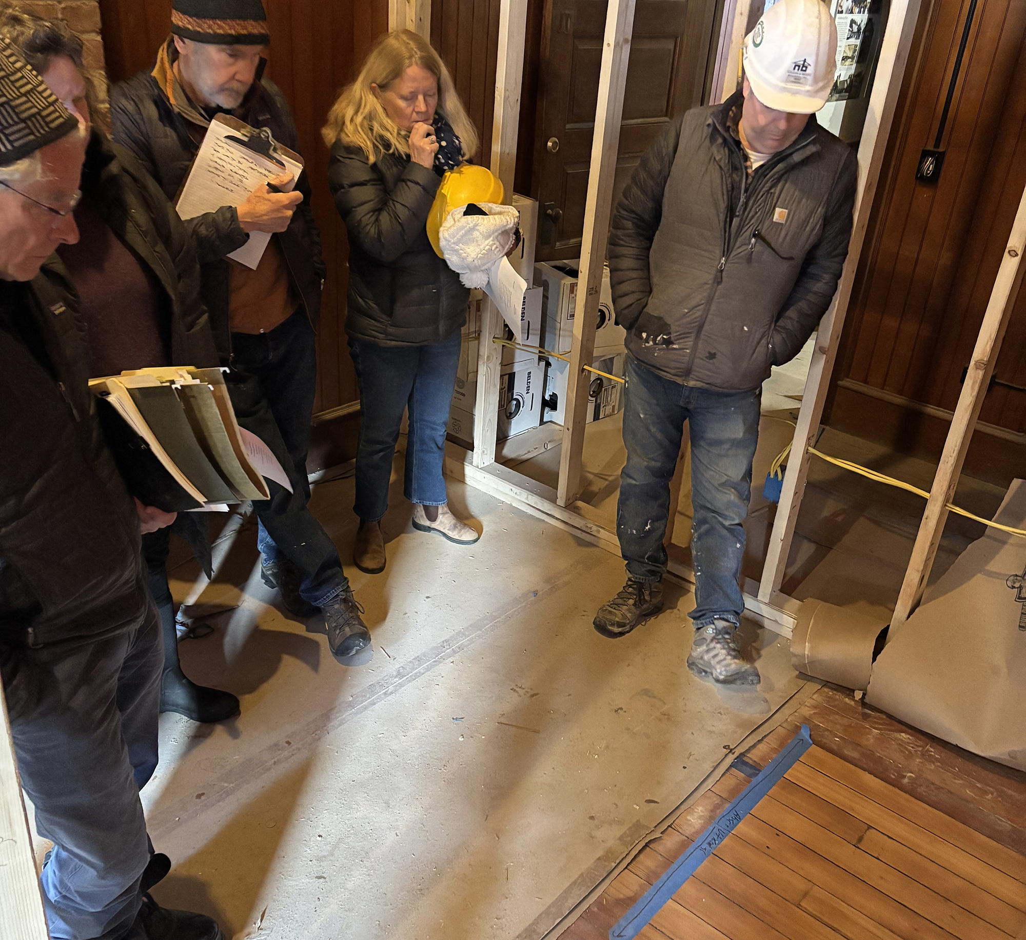 five people stare at varnished wood floor assessing a new varnish against the original