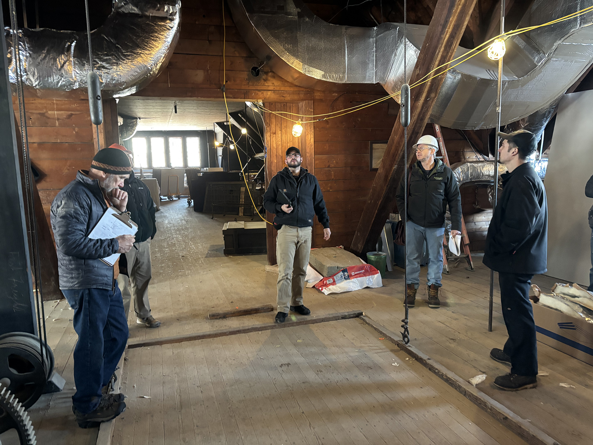 several men gathered around a wooden platform lift inside the Coach Barn to inspect it.