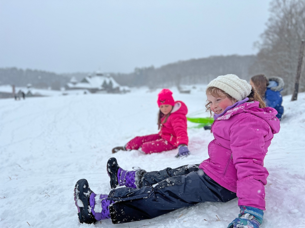 kids sit in the snow atop a hill