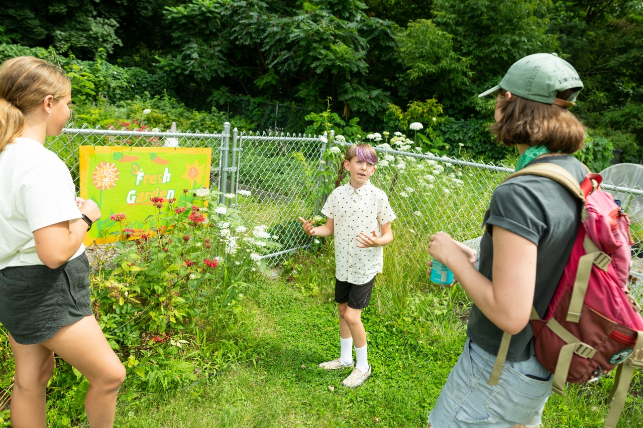 Two elementary aged children lead a tour through a blooming school garden in summertime.