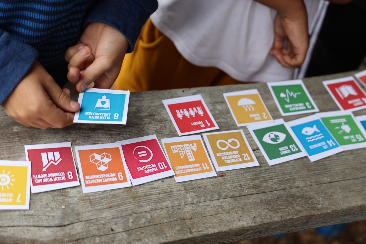 Colorful cards depicting the sustainable development goals are spread on a table and held by childrens hands