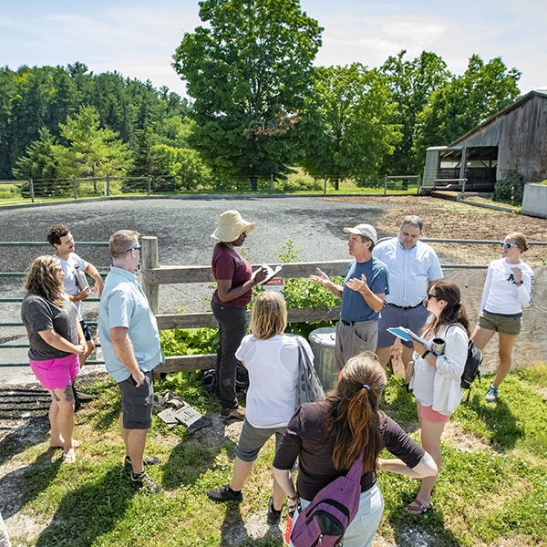 group of people gathered around man explaining biochar on manure pit behind them.