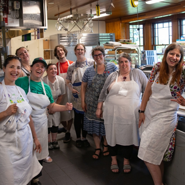 A group of adults in aprons smile in a restaurant kitchen