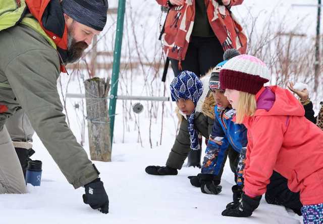 bearded man pointing out tracks in snow while 3 children look on