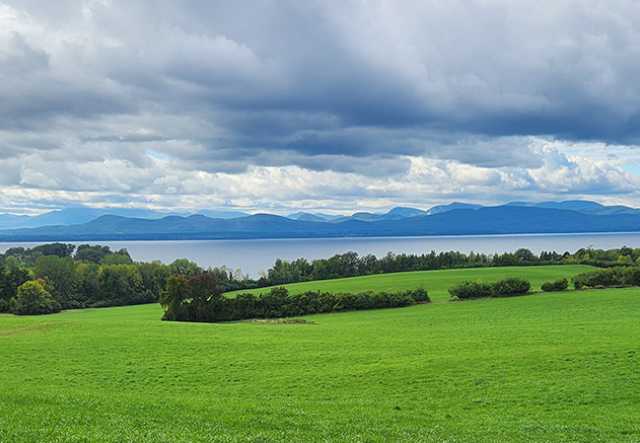 landscape of green fields, clouds, and lake and mountains in the background