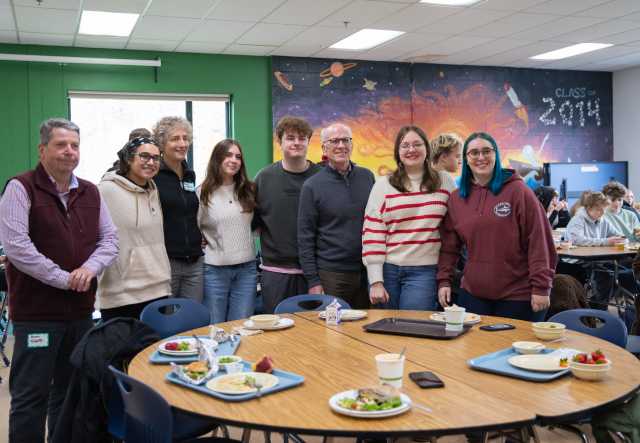 US Senator Peter Welch stands with four students in front of a mural with a space theme, smiling at the camera.