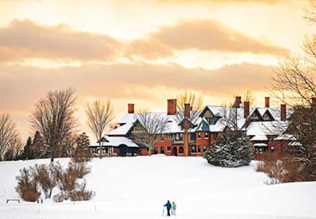 shelburne farms inn with snowy lawn and yellow-y sunset and clouds behind.