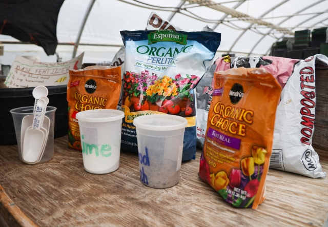 Bags of Espoma Organic Perlite and Miracle-Gro Organic Choice Potting Mix are on a wooden table in a greenhouse.