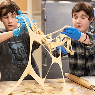 Two teenage boys stretch dough in an industrial kitchen