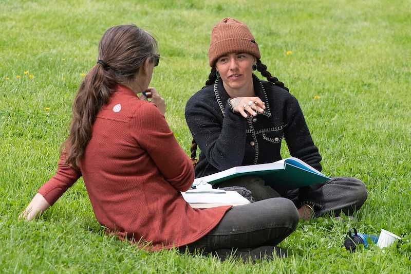 Two women sit on the grass talking