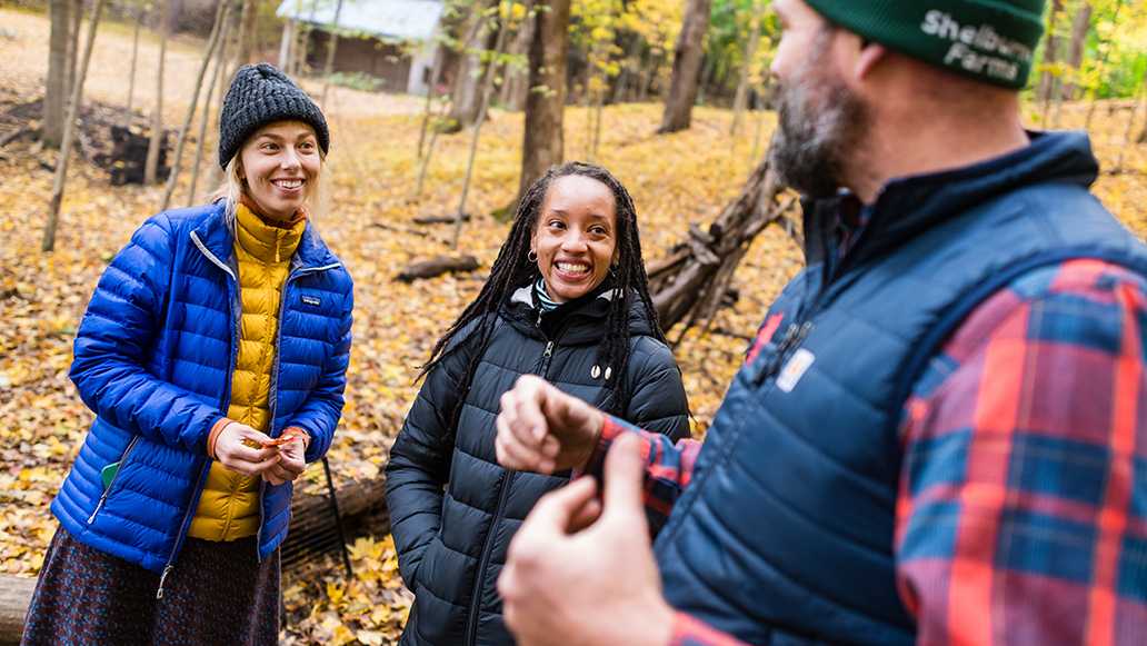 Three people talk during a workshop while standing in an autumn forest