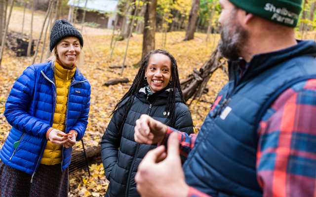 Three people talk during a workshop while standing in an autumn forest