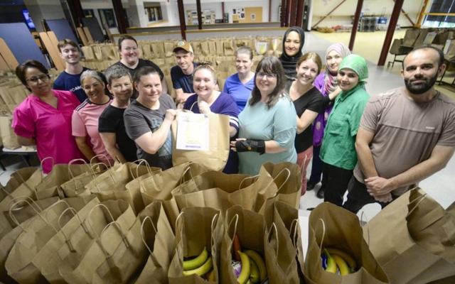 Group of school meals staff at a school cafeteria, standing behind rows of filled grocery bags.