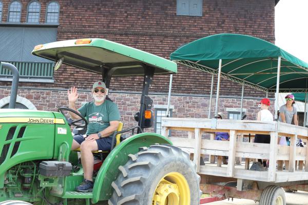 driver of tractor pulling a wagon of people waves at camera