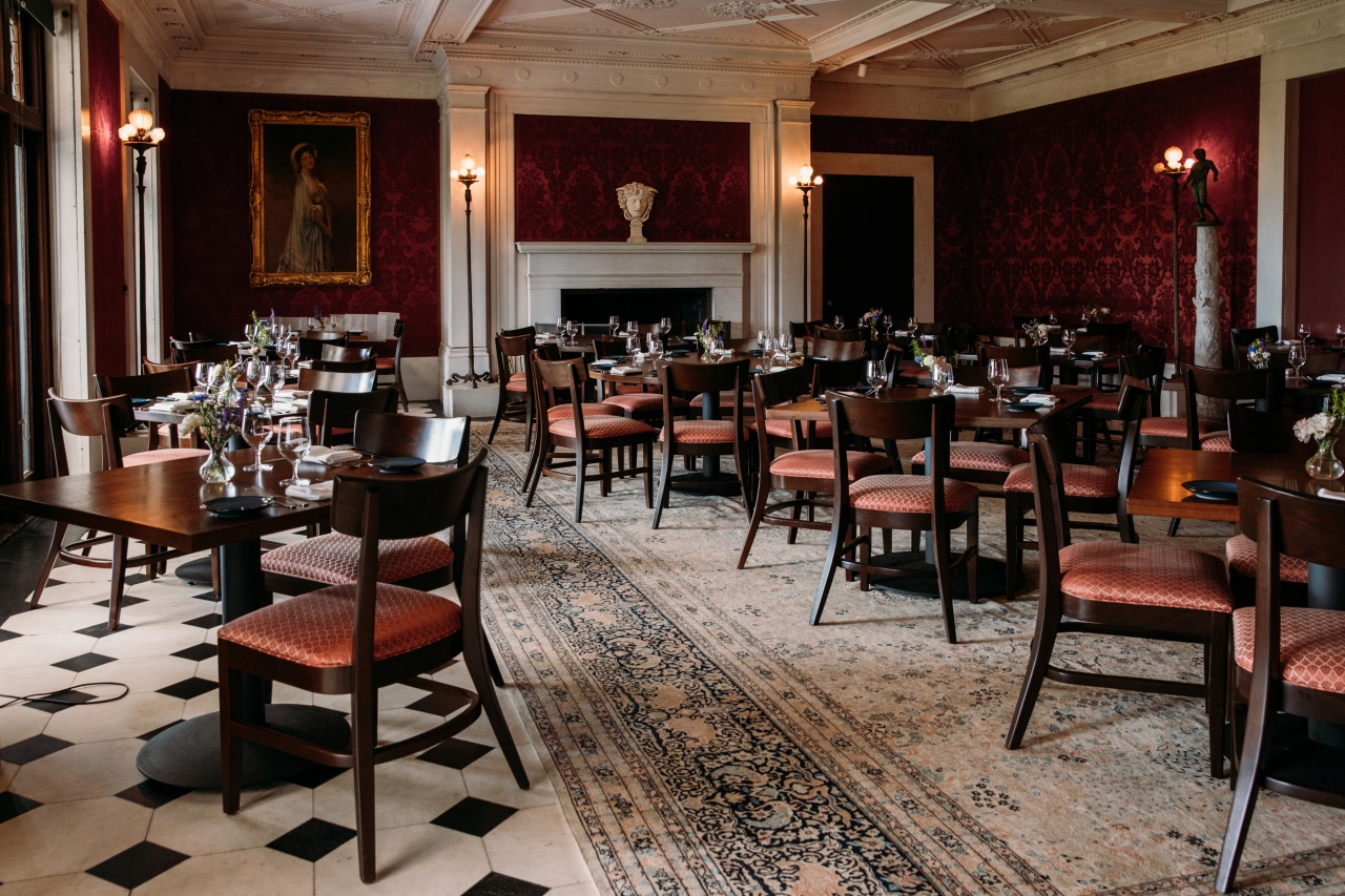 Interior shot of a dining room with ornate molding, deep red wallpaper, and rows of dark wood tables with dinner settings.