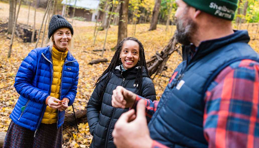 Three people talk during a workshop while standing in an autumn forest