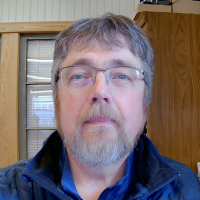 Man with gray hair and glasses smiles at a camera in an indoor setting.