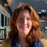 Woman with shoulder-length red hair smiles at the camera in front of a building exterior.