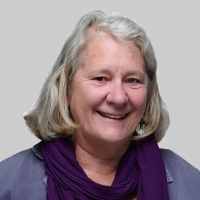 Woman with short gray hair smiles at camera in front of a gray background.