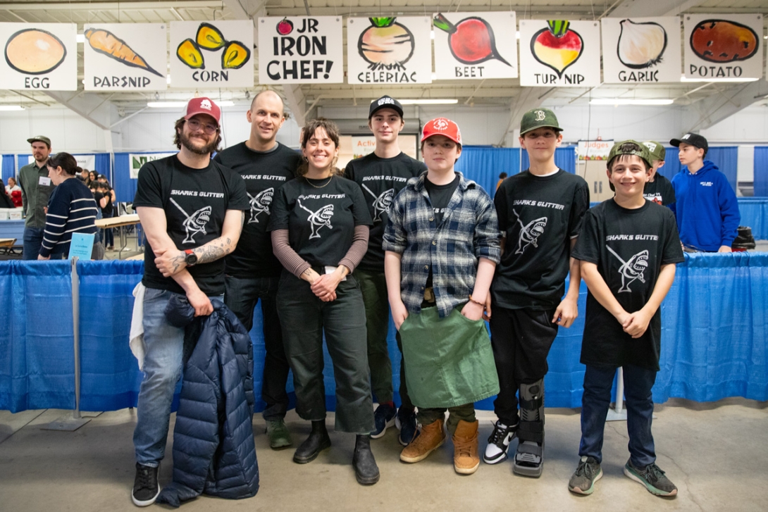 three adults and four middle school students stand for a group photo in an expo hall decorated with food-themed posters